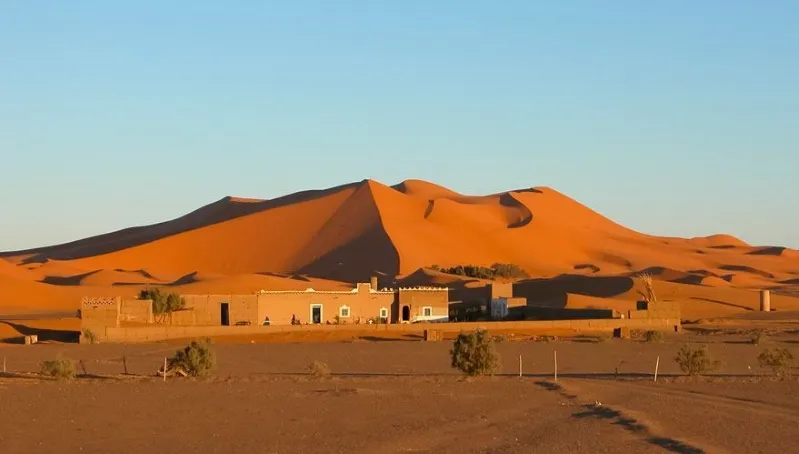A vast desert landscape of Erg Chebbi with a solitary house situated in the center.