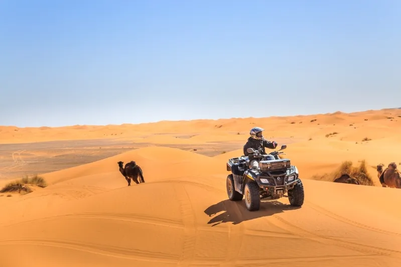 A man riding an ATV through the sandy landscape of the Merzouga desert under a clear blue sky.