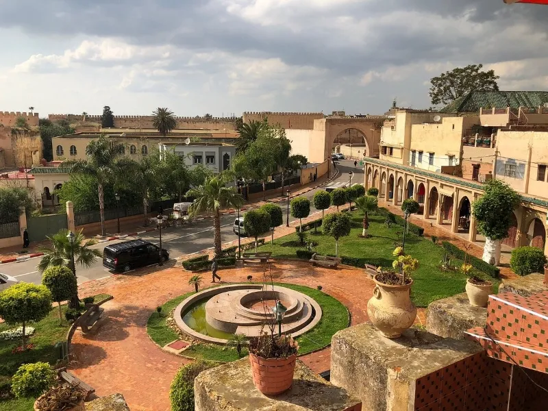 Un cour avec une fontaine et une voiture garée devant, dans le cadre du circuit des villes impériales marocaines.