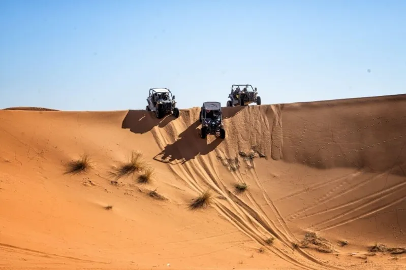 Quatre personnes en quad dans le désert du Maroc, évoluant sur un circuit desert maroc de sable doré sous un ciel bleu.