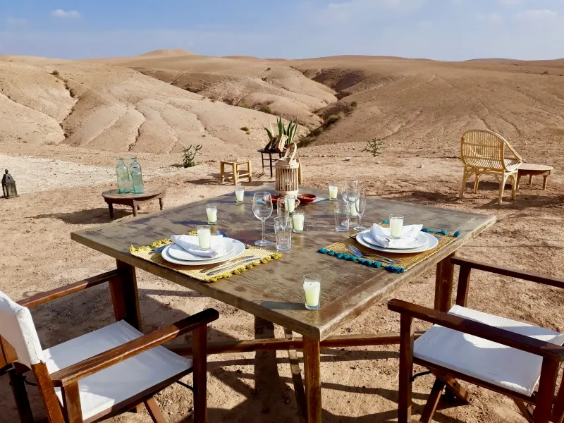 Une table élégamment dressée pour le dîner dans le désert d'Agafay, entourée de paysages arides et de dunes.
