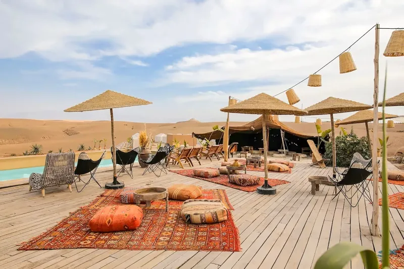 Une terrasse en bois avec une piscine et des parasols, située dans le paysage désertique d'Agafay.