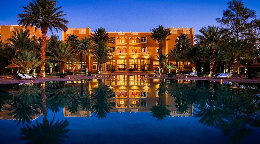 Vue nocturne d'un hôtel à Erfoud, Maroc, entouré de palmiers et d'une piscine.
