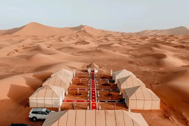 Un campement désertique avec des tentes et une voiture au centre, illustrant un voyage au Maroc.