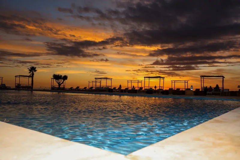 Une piscine au coucher du soleil, avec des teintes dorées et orangées illuminant le ciel en arrière-plan.visite maroc agence