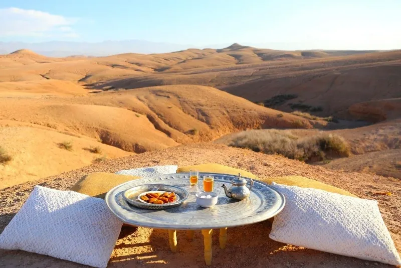 Un plateau de petit-déjeuner posé dans le désert marocain, entouré de dunes de sable et d'une lumière douce du matin.