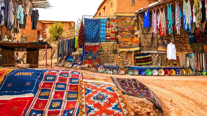 Un marché coloré à Erfoud, Maroc, présentant des tapis et divers articles colorés.