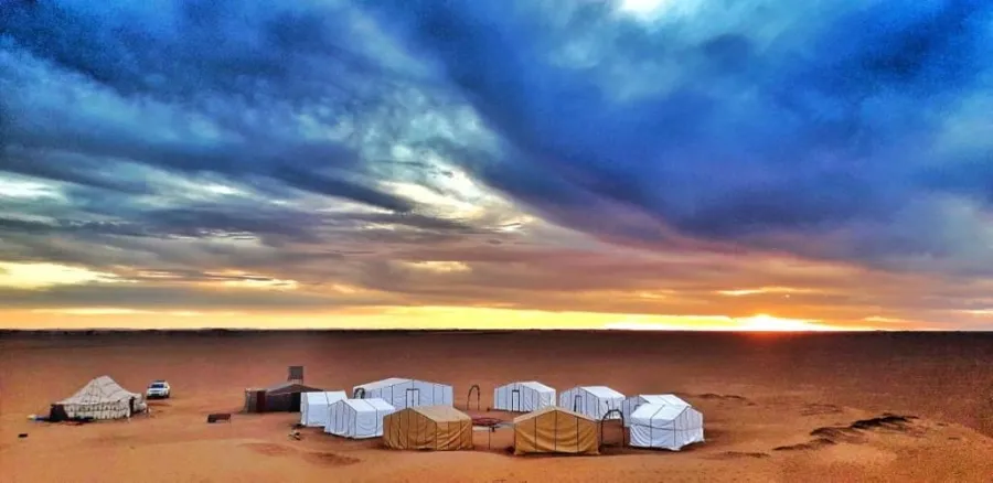 Tentes disposées dans le désert de M'hamid, Maroc, avec un ciel coloré au coucher du soleil en arrière-plan.