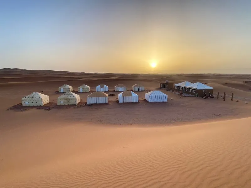 Un groupe de tentes dans le désert de M'hamid, au Maroc, illuminées par la lumière dorée du coucher de soleil.